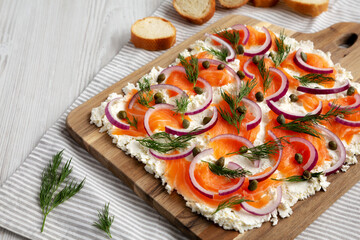 Homemade Cream Cheese Lox Bagel Board with Salmon on a white wooden surface, low angle view. Copy space.