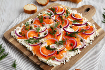 Homemade Cream Cheese Lox Bagel Board with Salmon on a white wooden surface, low angle view.