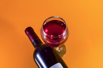 Bottle and glass of red wine on an orange background.