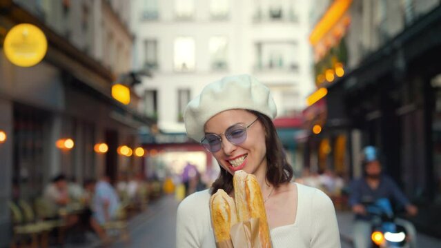 Young woman taking a bite of a French loaf from a bakery outdoors