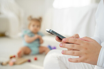 Close-up Young mom using smartphone while playing with baby. Lack of live communication, Addiction on gadgets. Social media, watch video, Working from home. App for kids goods.