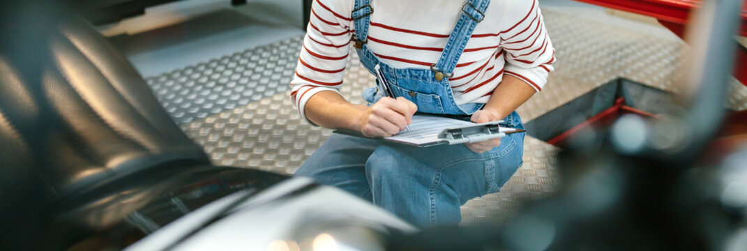 Unrecognizable mechanic woman with clipboard checking motorcycle and taking notes on factory - Powered by Adobe