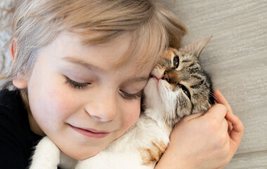 close-up of the face of a boy and a beloved kitten with closed eyes. cat day. Happy childhood with a furry purring friend. tricolor cat in the arms of a child. Favorite pets. selective focus