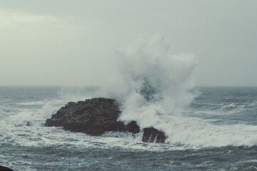 Splashing water over rock in ocean landscape photo. Beautiful nature scenery photography with grey sky on background. Idyllic scene. High quality picture for wallpaper, travel blog, magazine, article