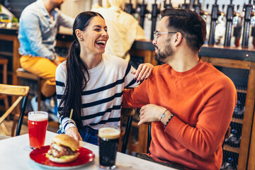Young couple in love having fun spending leisure time together at restaurant, eating burgers and drinking beer