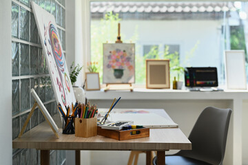 Artist studio interior with canvas, paint brushes, tubes of paint on wooden table. Painters room with tools and supplies