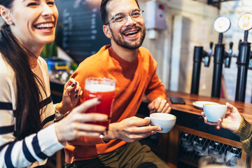 Smiling young friends drinking craft beer and coffee in pub