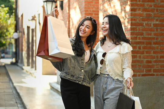Image of two young asian women talking, spending time together while walking in the shopping district of a city