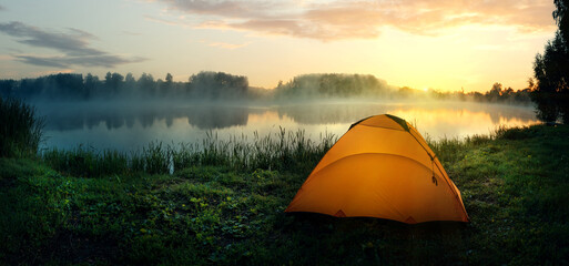 Orange tent on the bank of the river covered with fog in early morning