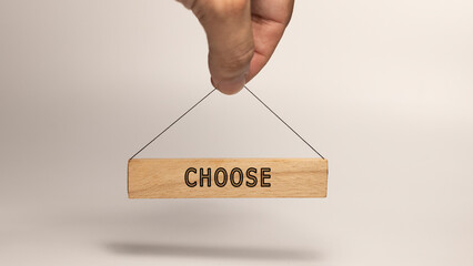 The word choose. Written on wooden sign hanging in human hand