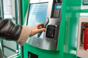 Close-up of a woman paying at a self-service machine using a contactless phone payment. Woman take...