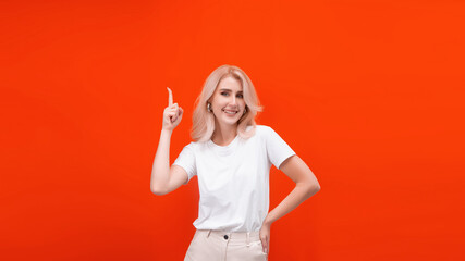 a blonde woman on an orange background in a white t-shirt stands and points with her hands with a smile