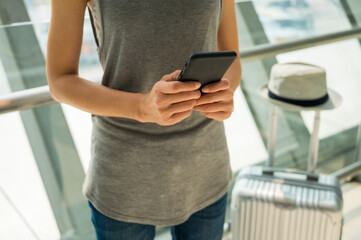 Close up female tourist using smartphone standing a trolley luggage is waiting to travel by plane. Travel concept