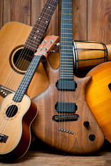 Fototapeta premium Acoustic and electric guitars, ukulele and djembe standing side by side on a wooden background.