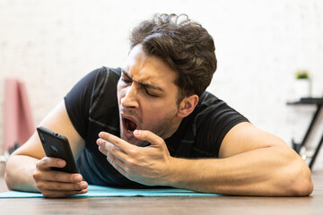 Tired young man yawning while training on the floor at home. Do sport and exercise at the morning time concept