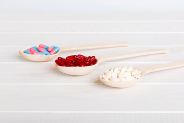 Vitamin capsules in a spoon on a colored background. Pills served as a healthy meal. Red soft gel vitamin supplement capsules on spoon