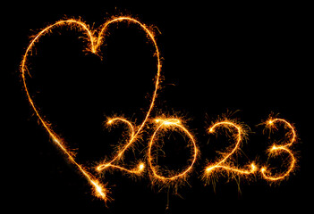 Herz und Jahreszahl 2023 mit strahlenden Wunderkerzen geschrieben vor schwarzem Hintergrund.