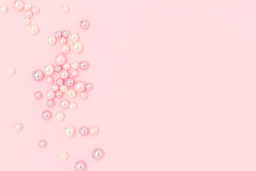 Multicolored imitation pearl beads scattered on a pink pastel background. Needlecraft creative...