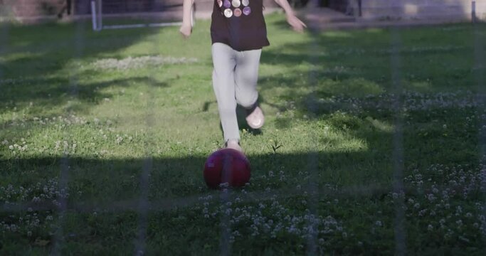 Little girl kicking the ball in soccer goal in backyard. Children play with a ball for football. Girl kicks the ball into the goal. Happy child kicks a ball on a green lawn.