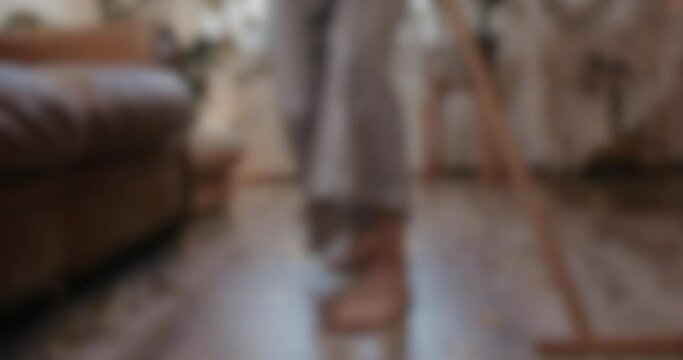 Woman listening to music and dancing while sweeping with a broom and doing house cleaning, blurred shot