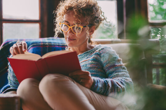 Woman at home sitting and reading a book in relax indoor leisure activity at home. Serene female people studying and read novel. Wearing glasses. Single lady lifestyle. Sunday time and vacation