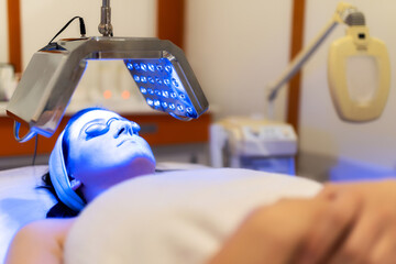 Facial treatment with led therapy. Girl on a light therapy procedure. LED lamp with blue light. Woman in protective glasses.