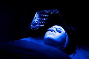 Young woman having blue LED light facial therapy treatment in beauty salon.
