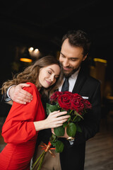 bearded man hugging happy girlfriend with bouquet of red roses on valentines day