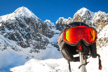 Ski helmet and googles on ski pole with snowy peaks at background