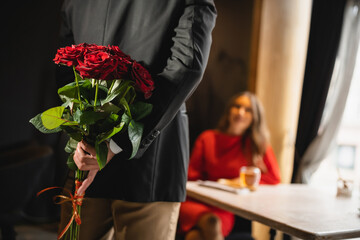 cropped view of man hiding bouquet of red roses behind back on valentines day