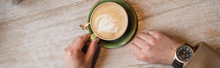 top view of cropped man holding cup of cappuccino with latte art, banner
