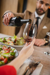 blurred man pouring red wine in glass of woman during dinner on valentines day