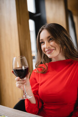 happy young woman holding glass with red wine and smiling in restaurant