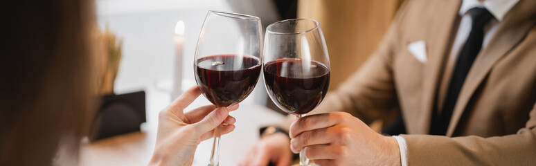 cropped view of couple clinking glasses with red wine during celebration on valentines day, banner