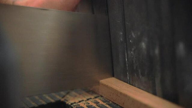 Man cutting raw wooden plank on two parts using hand saw, saw dust flying while cutting wooden profile. Man working with wood materials in workshop creating high quality furnitures and products