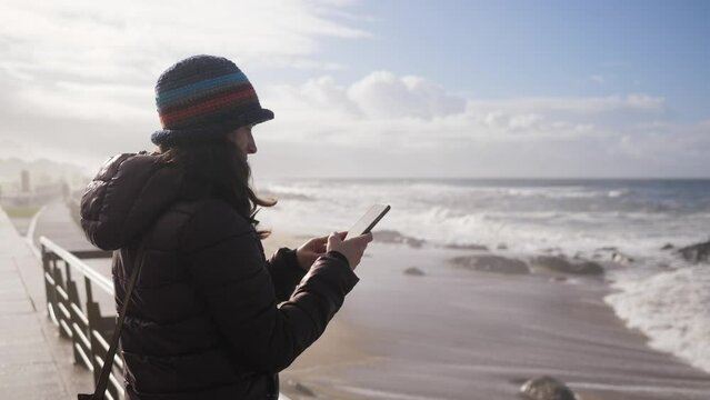 Woman tourist takes smartphone pictures of picturesque beautiful Atlantic ocean nature of Portugal coastline on winter time