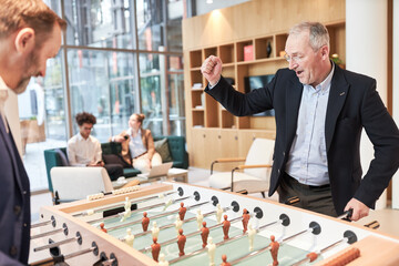 Businessman cheering while playing football at the foosball table