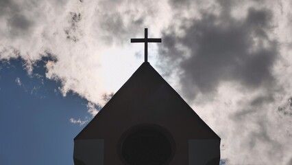 The silhouette of a Catholic church tower against a background of sun and clouds.