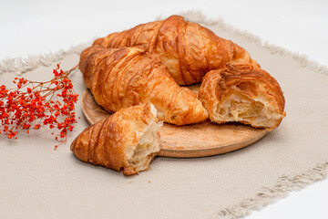 Croissants lie on a wooden textured plate on a jute textured napkin. French traditions.