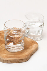 Two embossed  glasses with water  stand on a wooden stand on a white table.