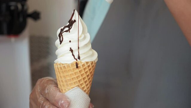 A close-up shot of the chef and the decoration of the ice cream with chocolate topping. yogurt ice cream in a waffle cone with chocolate topping. Pour chocolate sauce on top ice cream