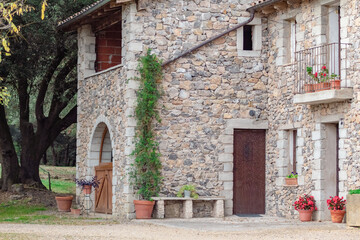 Fototapeta na wymiar Casa de piedra con muchas flores en las puertas plantadas en maceteros de diferentes tamaños de un pequeño pueblo de Girona con las puertas de madera.