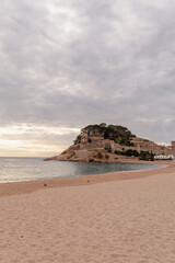 Panorámica de la playa de Tossa de Mar en Girona con el castillo sobre la montaña en el fondo bajo un cielo especial con nubes.