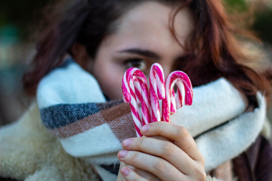 Mujer joven de raza caucásica de con el pelo corto y abrigada con una bufanda escondiéndose tras un grupo de bastones de caramelo de Navidad. 