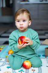 Fototapeta premium Portrait of a happy little boy with red apples. Little baby eating apple. Concept of health care and healthy child nutrition