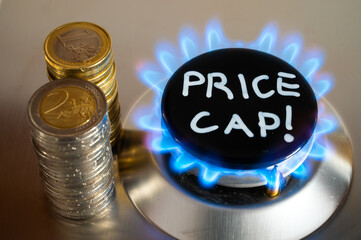 Lit gas stove, with coins next to it and Price Cap written. Introduction of the gas price limit in Europe.