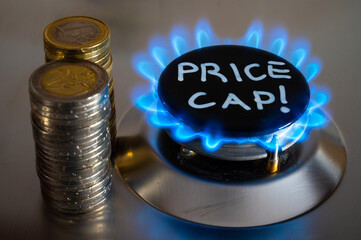 Lit gas stove, with coins next to it and Price Cap written. Introduction of the gas price limit in Europe.
