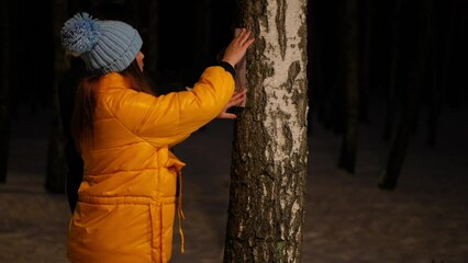 Side view young couple hanging lost pet announcement on tree in night park on winter. Troubled Asian man and Caucasian woman searching missing dog outdoors in darkness