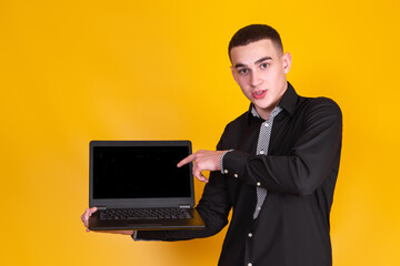 A handsome guy in a black shirt with a laptop on a yellow background