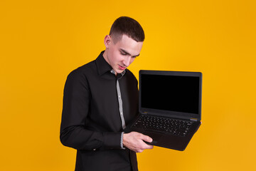 A handsome guy in a black shirt with a laptop on a yellow background